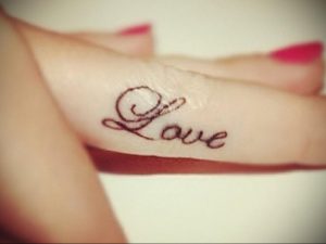 Фото татуировки надписи "Love" выполненной каллиграфическим шрифтом на пальце. Черно-белая татуировка, минималистичный дизайн, популярный выбор для девушек.