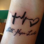 Фото тату на запястье: надпись 'Faith, Hope, Love' с символами креста, сердца и волны. Черно-белая татуировка, минимализм, религиозный символ.