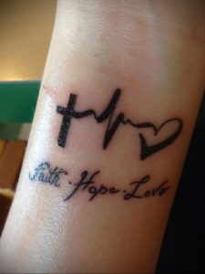 Фото тату на запястье: надпись 'Faith, Hope, Love' с символами креста, сердца и волны. Черно-белая татуировка, минимализм, религиозный символ.