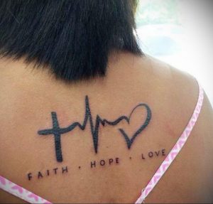 Фото тату на спине: надпись 'Faith, Hope, Love' с символами креста, сердца и волны. Черно-белая татуировка, минимализм, религиозный символ.
