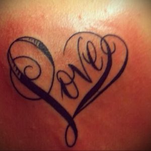Фото тату надписи 'Love' в форме сердца. Черно-серая татуировка с декоративными элементами и завитушками.