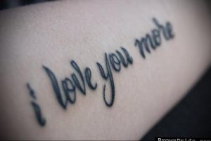 Фото тату надписи 'I Love You More' на руке. Черно-серая татуировка, выполненная каллиграфическим шрифтом, с акцентом на слове 'More'.