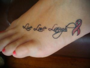 Фото тату надписи 'Live Love Laugh' с розовой лентой на стопе. Изящный шрифт и нежные цвета делают эту татуировку особенно привлекательной.
