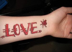 Фото тату: надпись 'Love' в ярком красном цвете, выполненная в стиле граффити с брызгами и контурами. Необычный и молодежный рисунок татуировки.