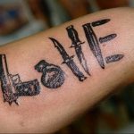 Фото тату: надпись 'Love', буквы которой заменены на изображения пистолета, ножа и пуль. Необычный и провокационный рисунок татуировки.