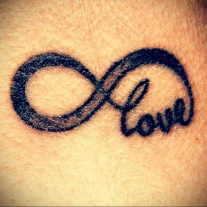 Фото тату: символ бесконечности с надписью 'Love' на запястье, выполненная черными чернилами. Изящный и минималистичный рисунок татуировки.