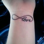 Фото тату с надписью 'Love' внутри символа бесконечности на запястье. Минималистичный рисунок татуировки черным цветом.