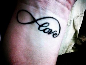 Фото тату на руке. Слово «Love» вписанное в символ бесконечности, черная татуировка, минималистичный стиль, идеи для девушек.