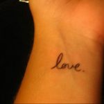 Фото татуировки с надписью 'love' на запястье. Простой и элегантный рисунок татуировки черным цветом.