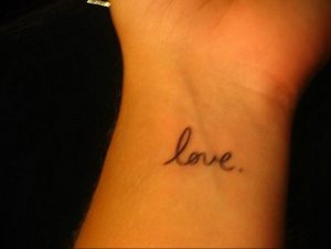 Фото татуировки с надписью 'love' на запястье. Простой и элегантный рисунок татуировки черным цветом.