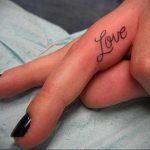 Фотография маленькой татуировки надписью 'Love' на пальце руки. Черный контур, минималистичный дизайн, популярные идеи для тату.