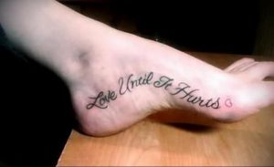 Фотография черной татуировки с надписью 'Love Until It Hurts' на стопе. Изящный шрифт и романтичный посыл.
