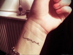 Фотография черной татуировки с надписью 'Love' на запястье. Минималистичный дизайн и изящный шрифт делают татуировку стильной и универсальной.