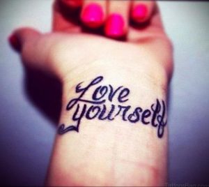 Фотография черной татуировки с надписью 'Love Yourself' на запястье. Элегантный шрифт и позитивный посыл.