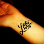 Фотография черной татуировки с надписью 'Love' на запястье. Простой, но элегантный шрифт делает татуировку стильной и универсальной.