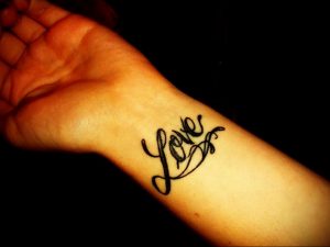 Фотография черной татуировки с надписью 'Love' на запястье. Простой, но элегантный шрифт делает татуировку стильной и универсальной.