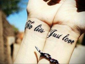 Фото парных татуировок на запястьях с надписью 'No Lies Just Love' выполненных черными чернилами. Изящный шрифт и минималистичный дизайн.