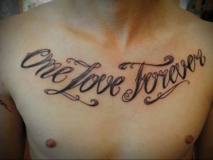 Фото тату на груди: надпись 'One Love Forever' в каллиграфическом стиле с декоративными элементами. Романтический и изысканный дизайн.