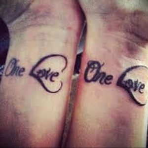 Фото парных татуировок на запястьях: надпись 'One Love' и контур сердца, разделенные между двумя людьми. Романтический и символичный дизайн.