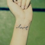 Фото тату на запястье: простая надпись 'love' черным контуром. Минималистичный стиль, элегантный дизайн.