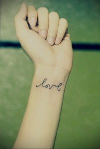 Фото тату на запястье: простая надпись 'love' черным контуром. Минималистичный стиль, элегантный дизайн.