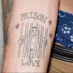 Фото тату на предплечье: рисунок заключенного за решеткой с надписями 'Prison' и 'Love', украшенного сердечками. Необычный и провокационный дизайн.