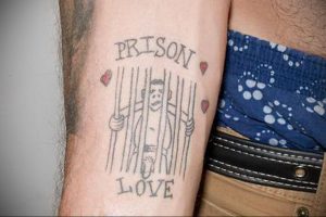 Фото тату на предплечье: рисунок заключенного за решеткой с надписями 'Prison' и 'Love', украшенного сердечками. Необычный и провокационный дизайн.