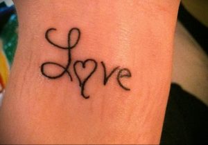 Фотография небольшой татуировки на запястье с надписью 'Love', где буква 'o' заменена на сердце.