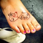 Фото татуировки на стопе с надписью 'Love', вписанной в символ бесконечности, с добавлением декоративных элементов.
