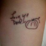 Фото тату на руке с изображением детского рисунка надписи 'Love you Dad' и тыквы. Простой и наивный стиль.
