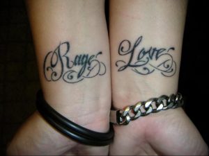 Фотография парных татуировок на запястьях с надписями 'Rage' и 'Love'. Татуировки выполнены черными линиями в каллиграфическом стиле.