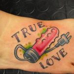 Фото татуировки на стопе с изображением шприца и надписи 'True Love'. Татуировка выполнена в ярких цветах, с использованием традиционного стиля.