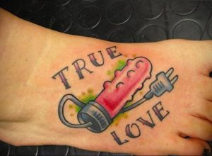 Фото татуировки на стопе с изображением шприца и надписи 'True Love'. Татуировка выполнена в ярких цветах, с использованием традиционного стиля.