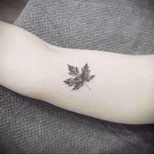 Фото тату: маленький, реалистичный кленовый лист, выполненный в технике blackwork, на внутренней стороне предплечья.