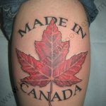 Фото тату кленового листа на бедре с надписью 'Made in Canada'. Рисунок выполнен в реалистичном стиле с использованием красных и коричневых оттенков.