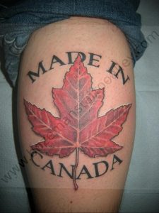 Фото тату кленового листа на бедре с надписью 'Made in Canada'. Рисунок выполнен в реалистичном стиле с использованием красных и коричневых оттенков.