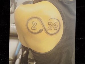 Фото тату бесконечность на плече с цифрами '2' и '24' внутри. Рисунок татуировки, выполненный в черно-серых тонах.