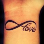 Фото тату бесконечность на запястье с надписью 'Love' внутри. Минималистичный рисунок татуировки, выполненный черными чернилами.