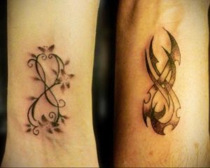 Фото парных татуировок бесконечности на запястьях. Одна татуировка украшена цветами и листьями, другая – геометрическим узором. Черно-серые тона.