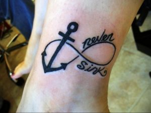 Фото тату бесконечность с якорем и надписью 'never sink' на предплечье. Черно-белый рисунок татуировки в минималистичном стиле.