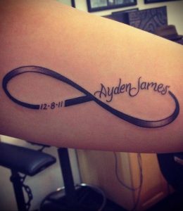 Фото тату бесконечность на предплечье с надписью 'Ayden James' и датой '12.8.11'. Черно-белый рисунок татуировки в минималистичном стиле.