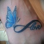 Фото тату на руке: символ бесконечности, в котором заключено слово 'Love', и яркая голубая бабочка. Красочный и романтичный рисунок татуировки.