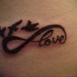 Фото тату на руке: символ бесконечности, в котором заключено слово 'Love', и две летящие птицы. Романтичный и символичный рисунок татуировки.