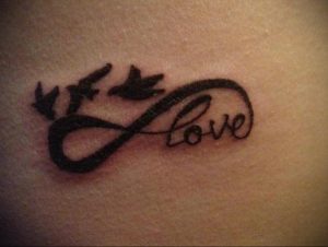 Фото тату на руке: символ бесконечности, в котором заключено слово 'Love', и две летящие птицы. Романтичный и символичный рисунок татуировки.