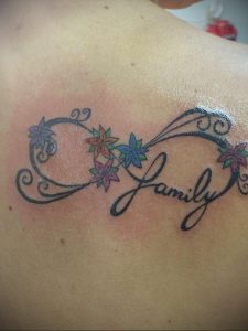 Фото тату на спине: знак бесконечности, украшенный цветами, и надпись 'Family'. Цветная татуировка, символ любви и преданности семье.