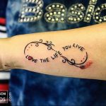 Фото тату бесконечности на руке с надписью 'love the life you live'. Черно-красный рисунок татуировки, символизирующий любовь к жизни.