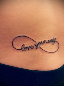 Фото тату: минималистичная татуировка бесконечности на боку с надписью 'love yourself', выполненная тонкими черными линиями.