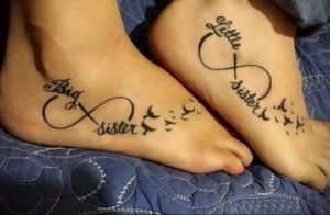 Фото парных тату бесконечность с летящими птицами и надписями 'Big Sister' и 'Little Sister' на стопах.