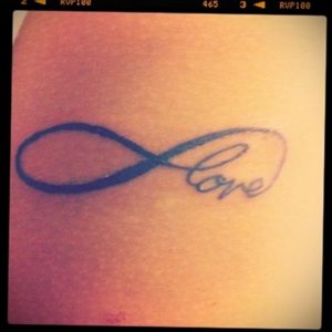 Фото татуировки на руке с изображением символа бесконечности и надписью 'Love'. Минималистичный дизайн, выполненный в синих тонах.