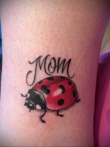 Фото тату божьей коровки с надписью "Mom" на руке. Нежный и трогательный рисунок, посвященный матери.
